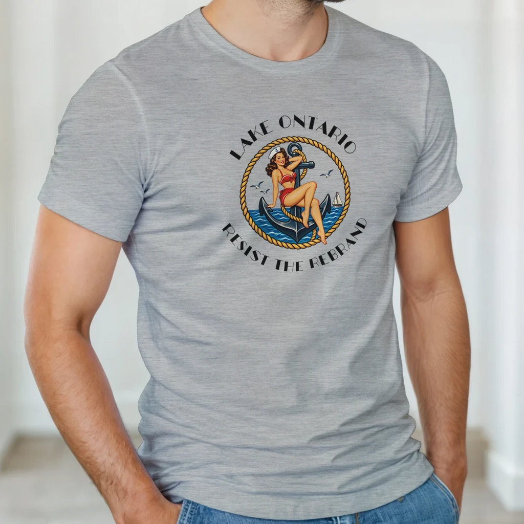 A man wearing light heather gray short-sleeve t-shirt with a vintage-style circular graphic on the chest. The graphic features a pin-up illustration of a woman in a red bikini  seated on a blue anchor, with the text 'LAKE ONTARIO' above and 'Resist the Rebrand' below in black.