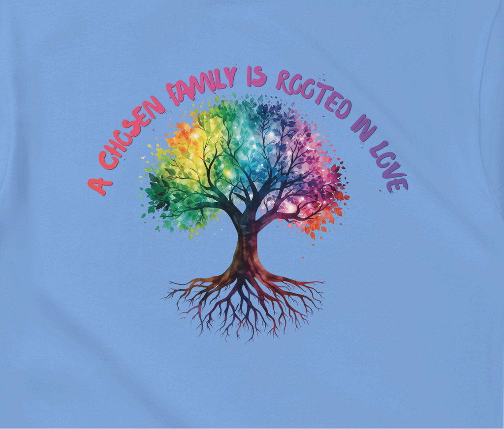 A Carolina Blue t-shirt featuring a colorful graphic of a tree with a rainbow-colored canopy and roots, with the text 'A Chosen Family is Rooted in Love' arched above it in pink and purple lettering.