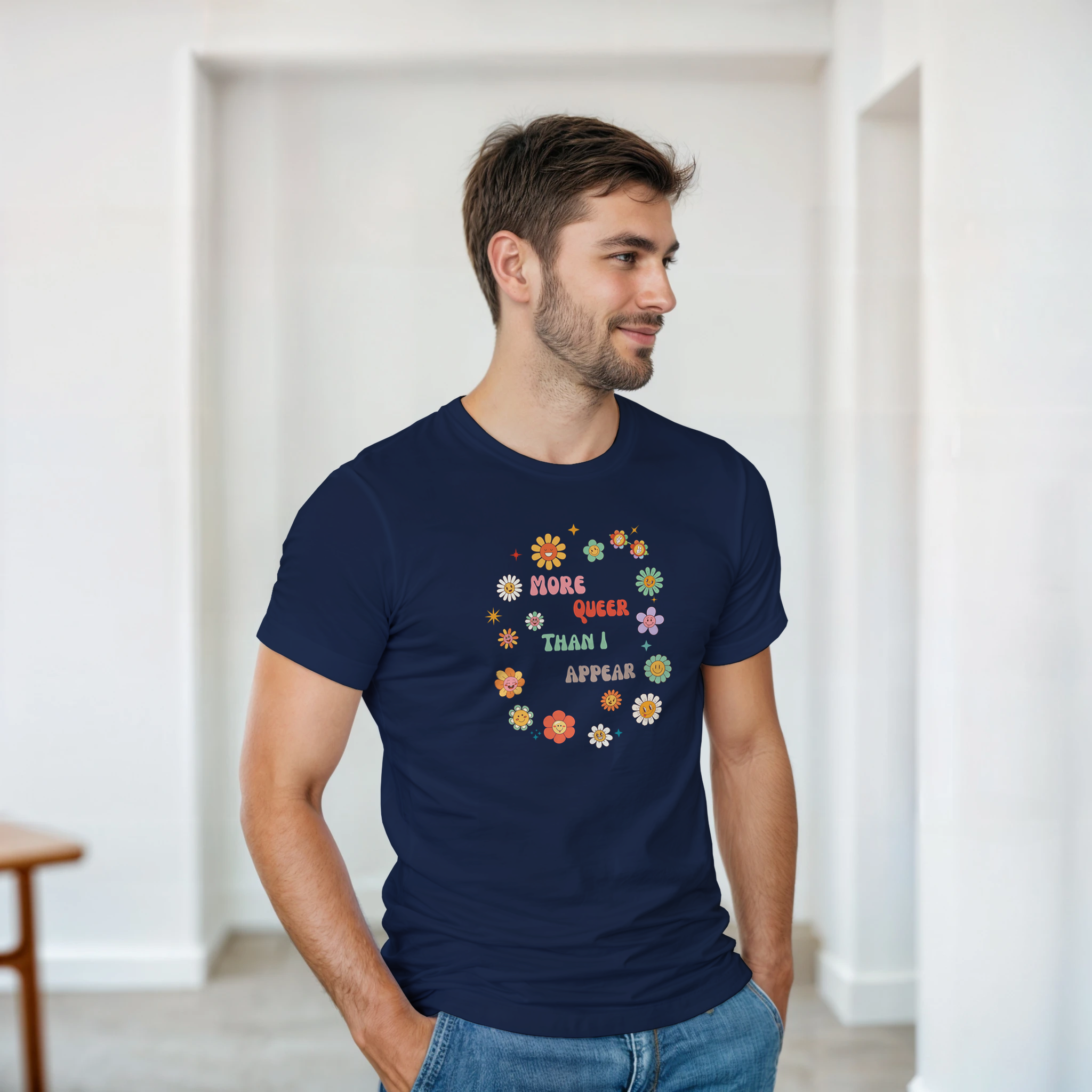 A navy tee with a graphic design featuring the text 'More queer than I appear' in a playful, retro font, surrounded by a circle of smiling, colorful flowers.
