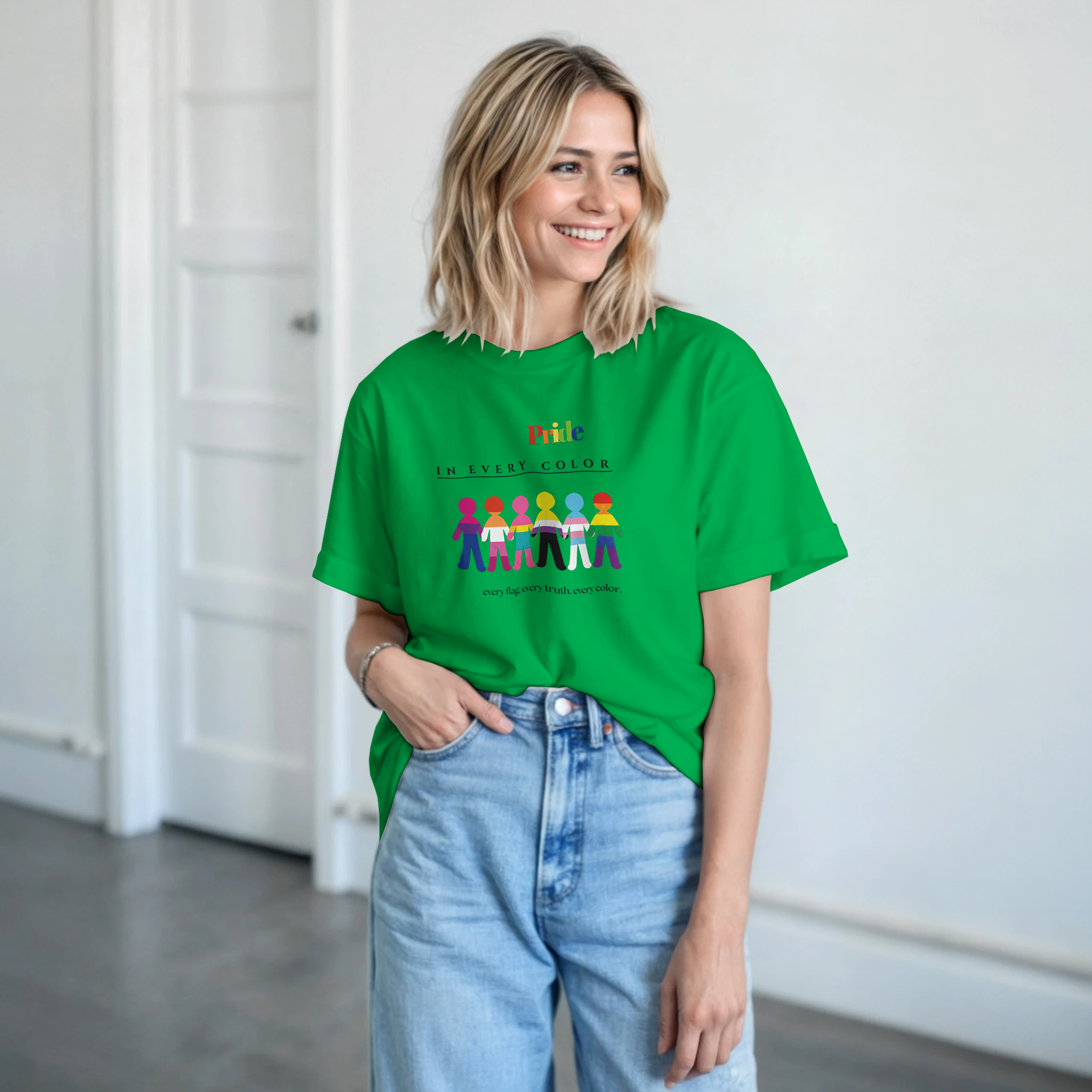A woman wearing an irish green tee with a message Pride in Every Color followed by design of paper doll chain, each in a different pride flags colors.  Underneath is the wording, 'every flag. every truth. every color.