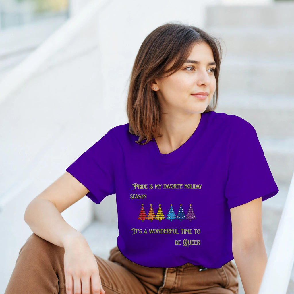 A woman wearing a purple shirt with a row of rainbow colored Christmas trees with the words, "Pride is my favorite Holiday Season. It's a wonderful time to be queer".