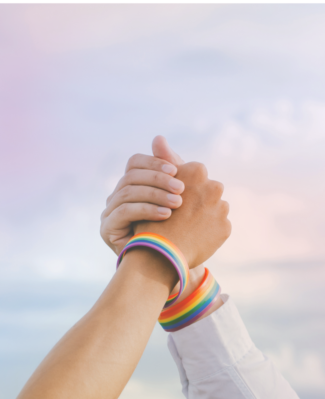 Two people holding hands both wearing Pride wristbands.